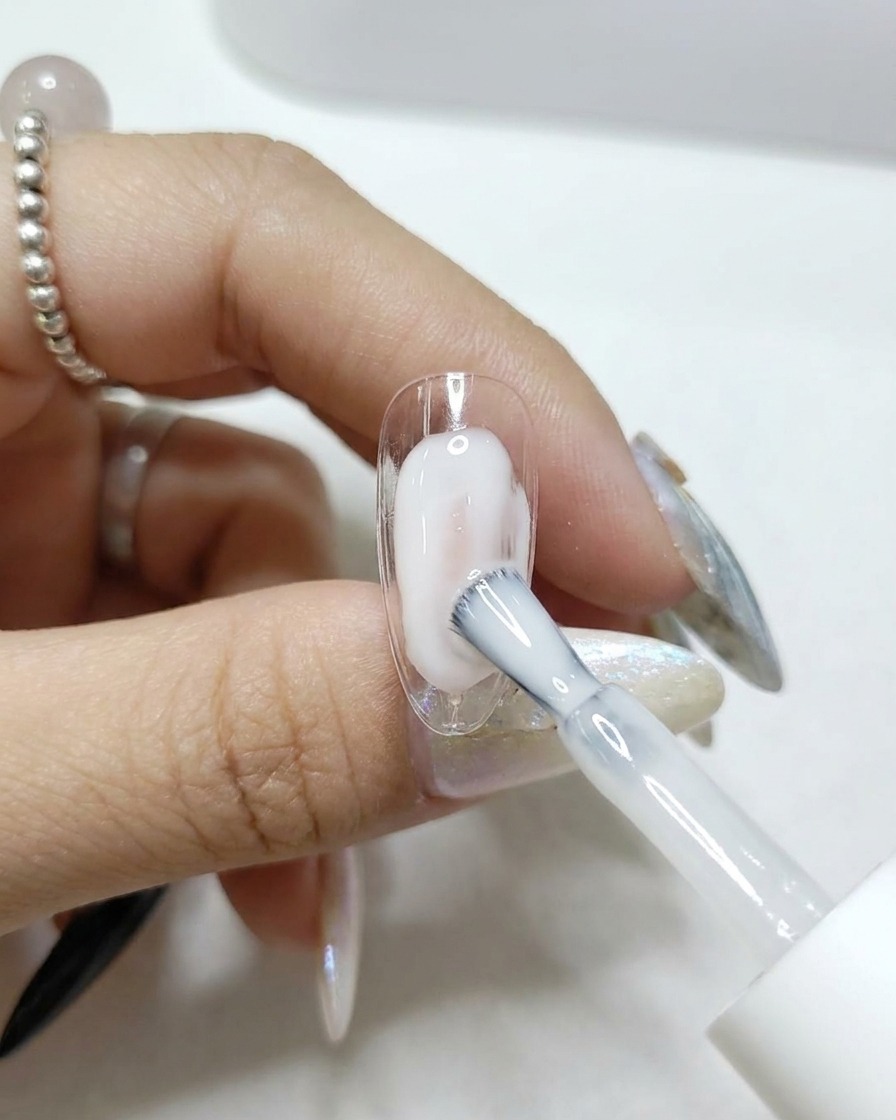 透明なネイルチップにクリアで光沢のあるトップコートを塗布している様子。