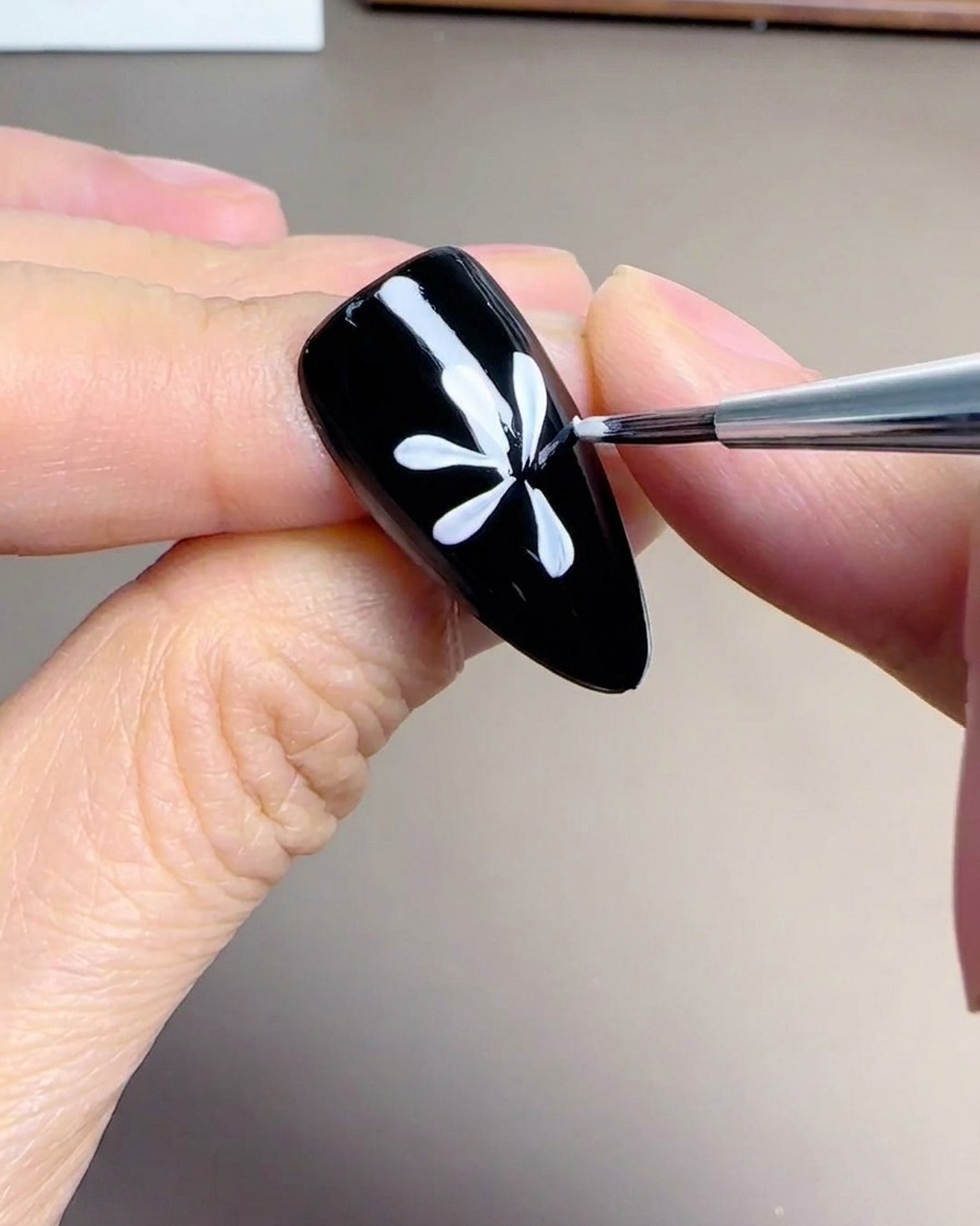 黒いネイルの上に描かれた、円形に並ぶデイジーの花びら。