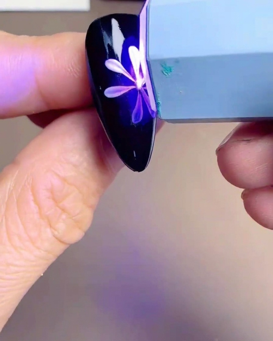 UV/LEDランプの下で、白いデイジーと黄色い花芯が描かれたネイルチップが照らされている。