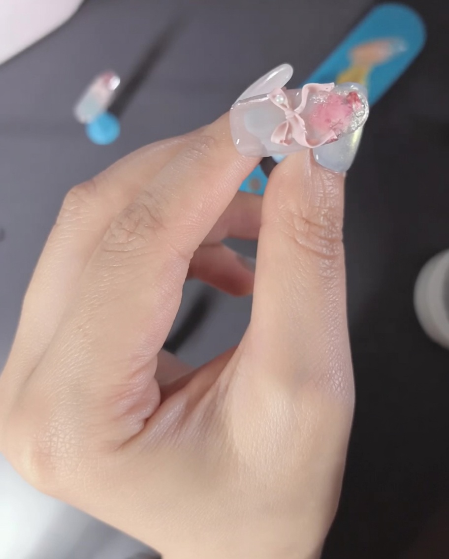 ピンクの3Dリボンパーツとパールで飾られた指のクローズアップ