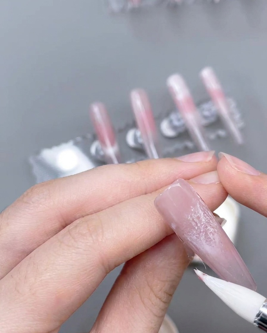 装飾された爪の上に、細いライナーブラシを使って繊細なピンクのアクセントラインを描いている様子