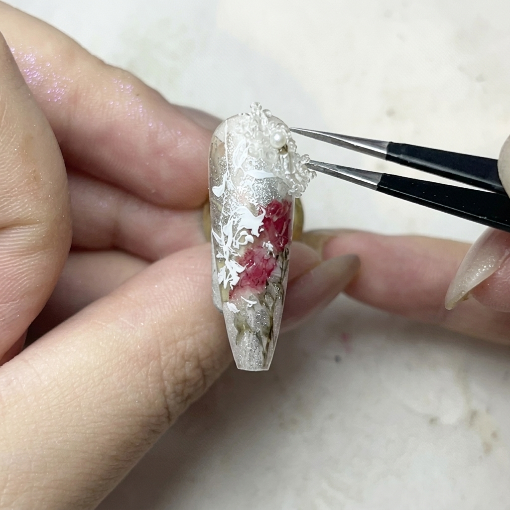 ピンセットで小さな白い3Dフラワーをジェルに乗せている様子。