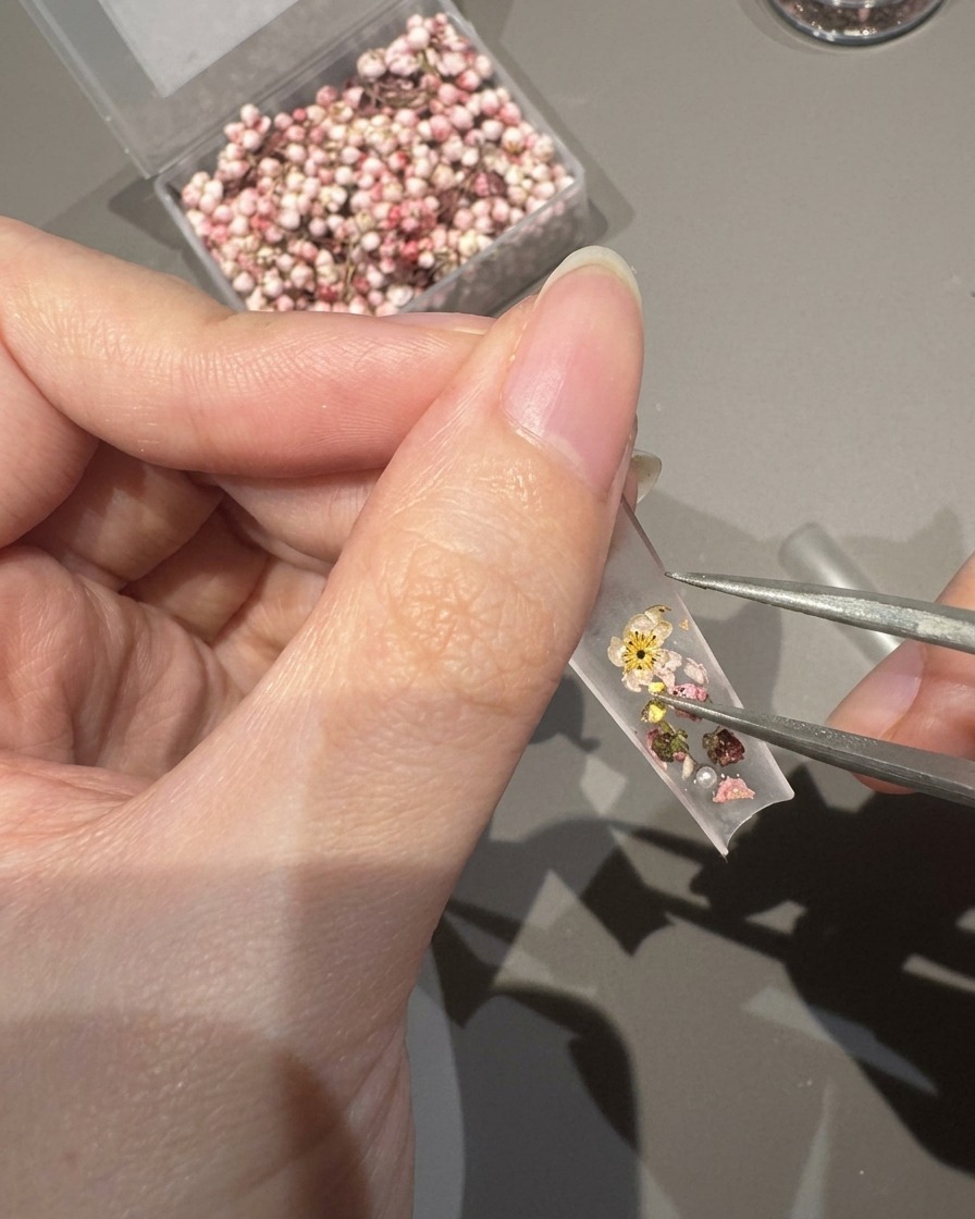 押し花の隙間に小さなパールとクリスタルをピンセットで置いている様子。