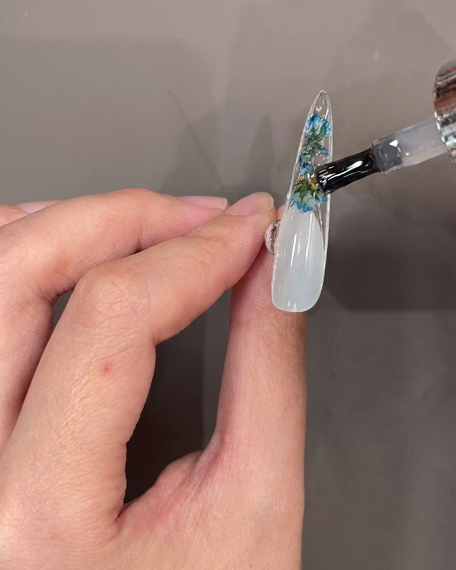 装飾されたチップの裏面にトップジェルを塗り、仕上げている様子。