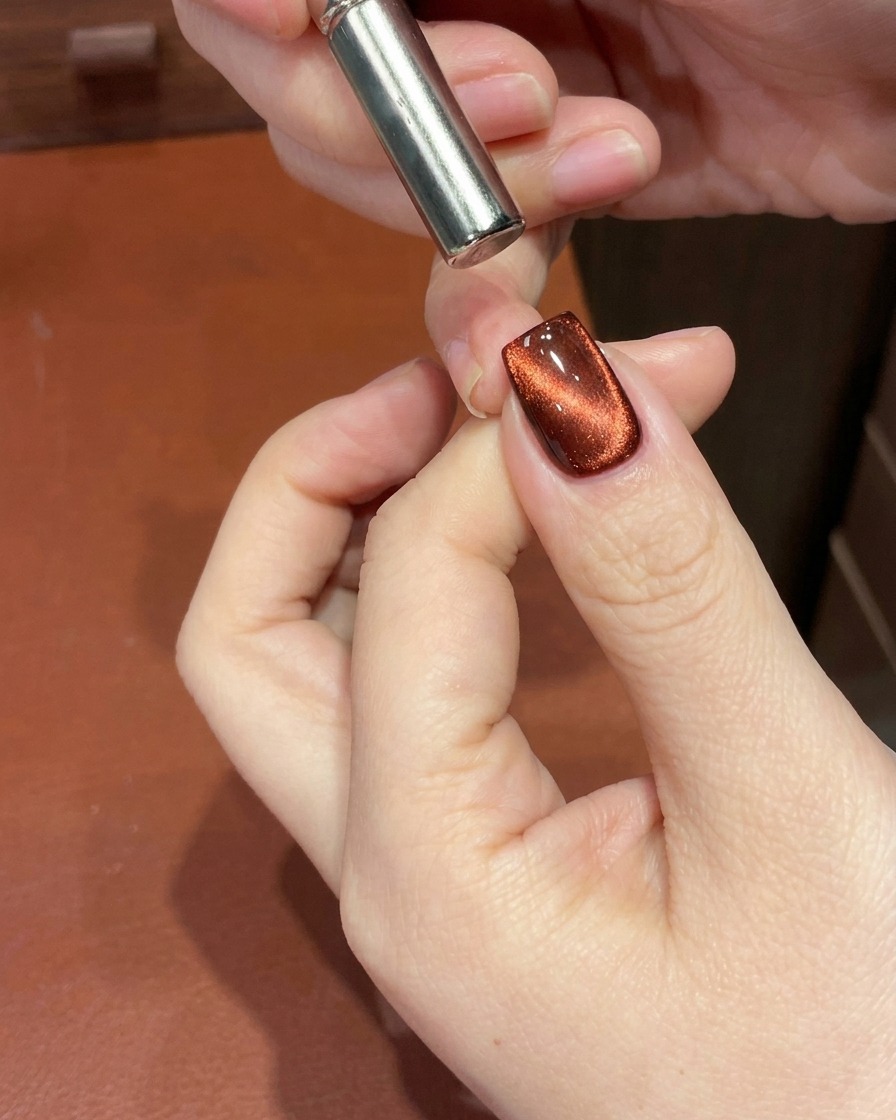 キューティクル付近でマグネットを使用し、キャッツアイの輝きを深いグラデーションに変化させている、赤いマグネットネイルのクローズアップ。