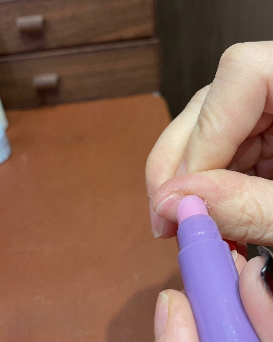 完成したマニキュアの表面とエッジを優しく滑らかにするためにキューティクルケアペンを使用しているクローズアップ。
