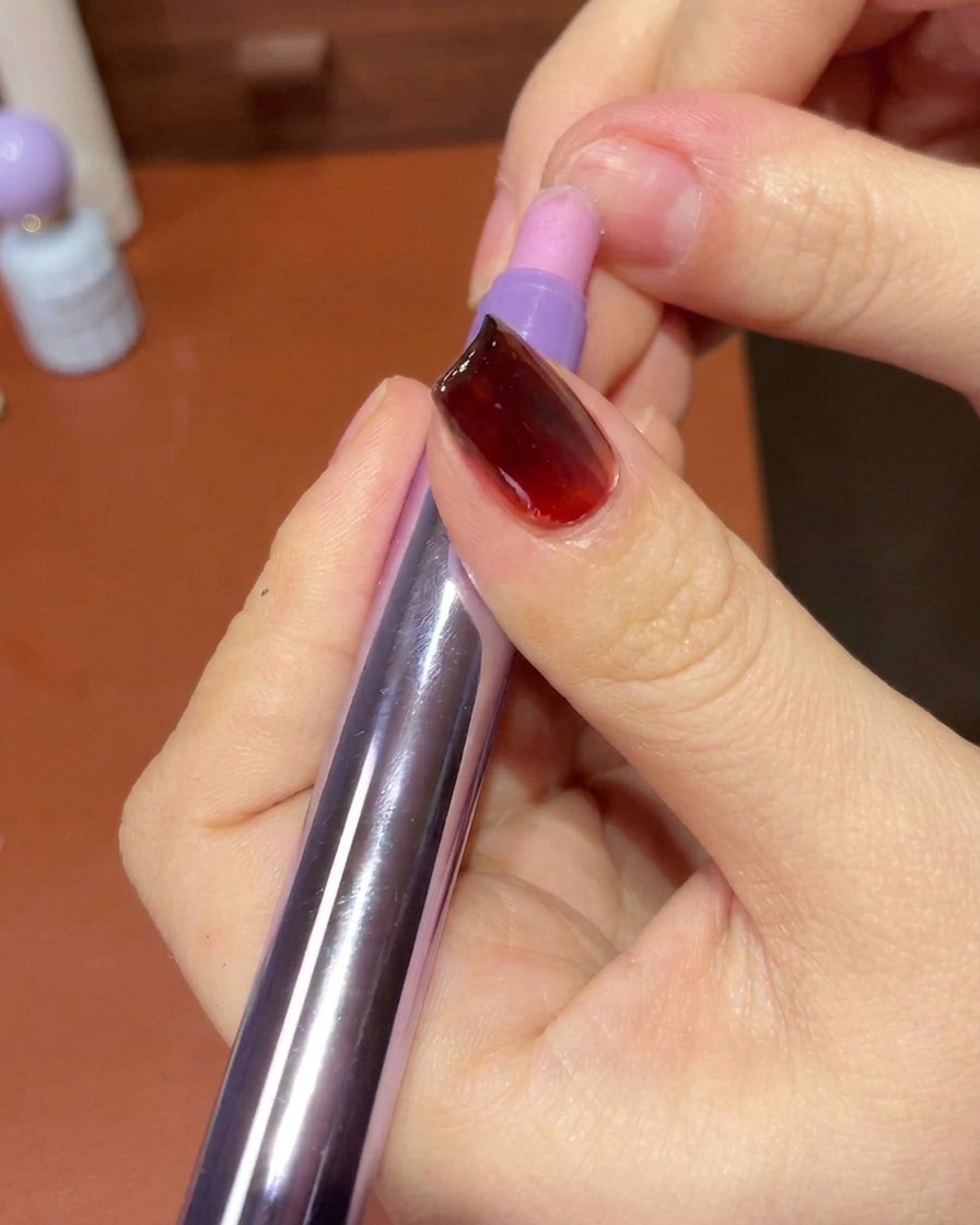 糸くずの出ないワイプを使って、完成したジェルネイルの爪周りの皮膚やエッジを綺麗に拭き取っている手元。