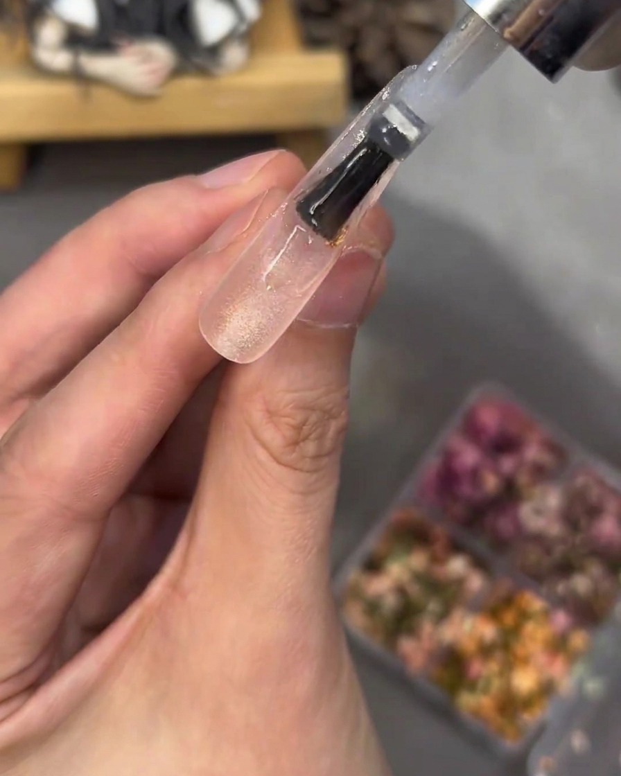 花やストーンの上から厚みのあるクリアジェルを塗って埋め込んでいる様子