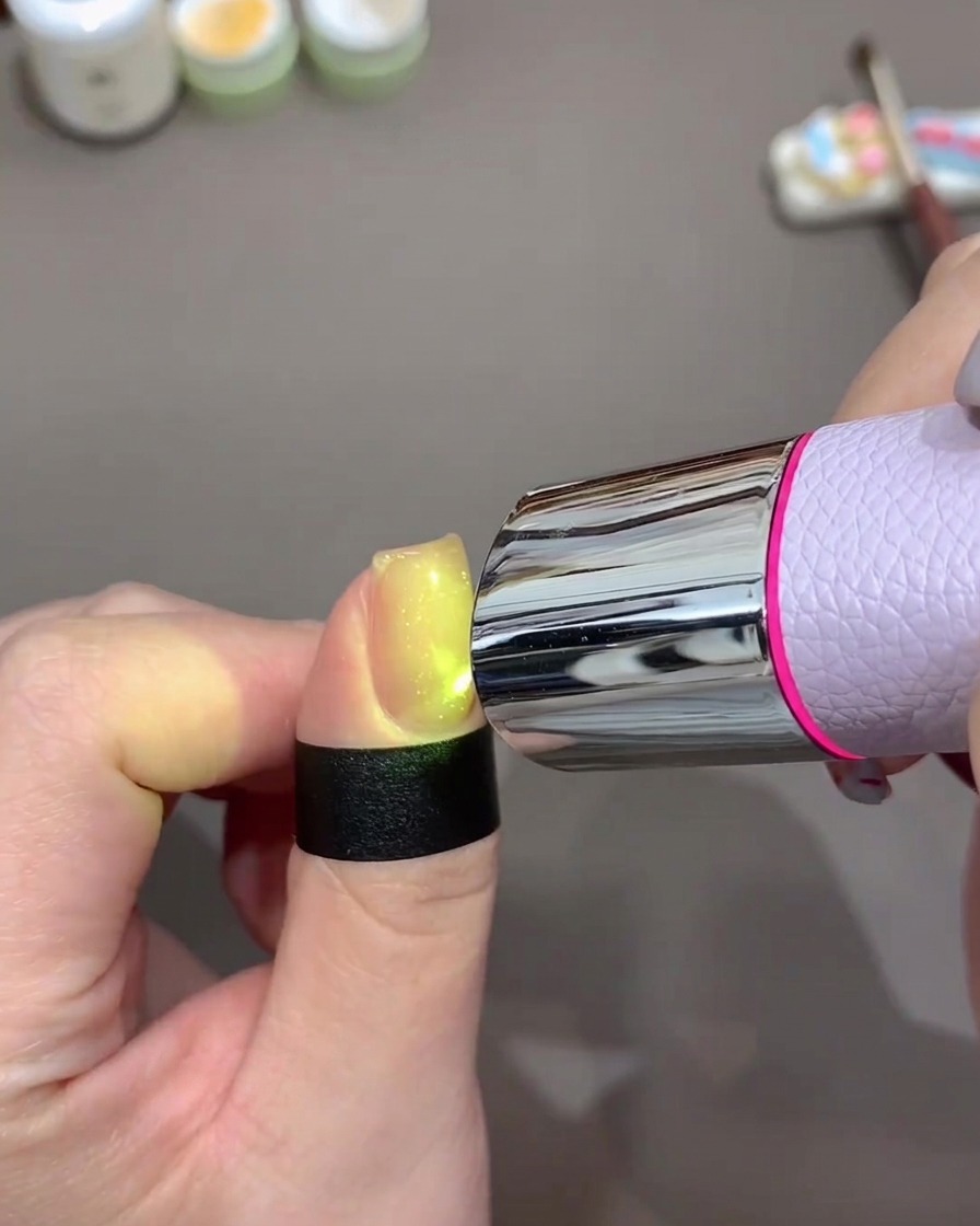 持ち運び可能な小型のパープルUV/LEDライトの下で、ジェルが硬化している様子。
