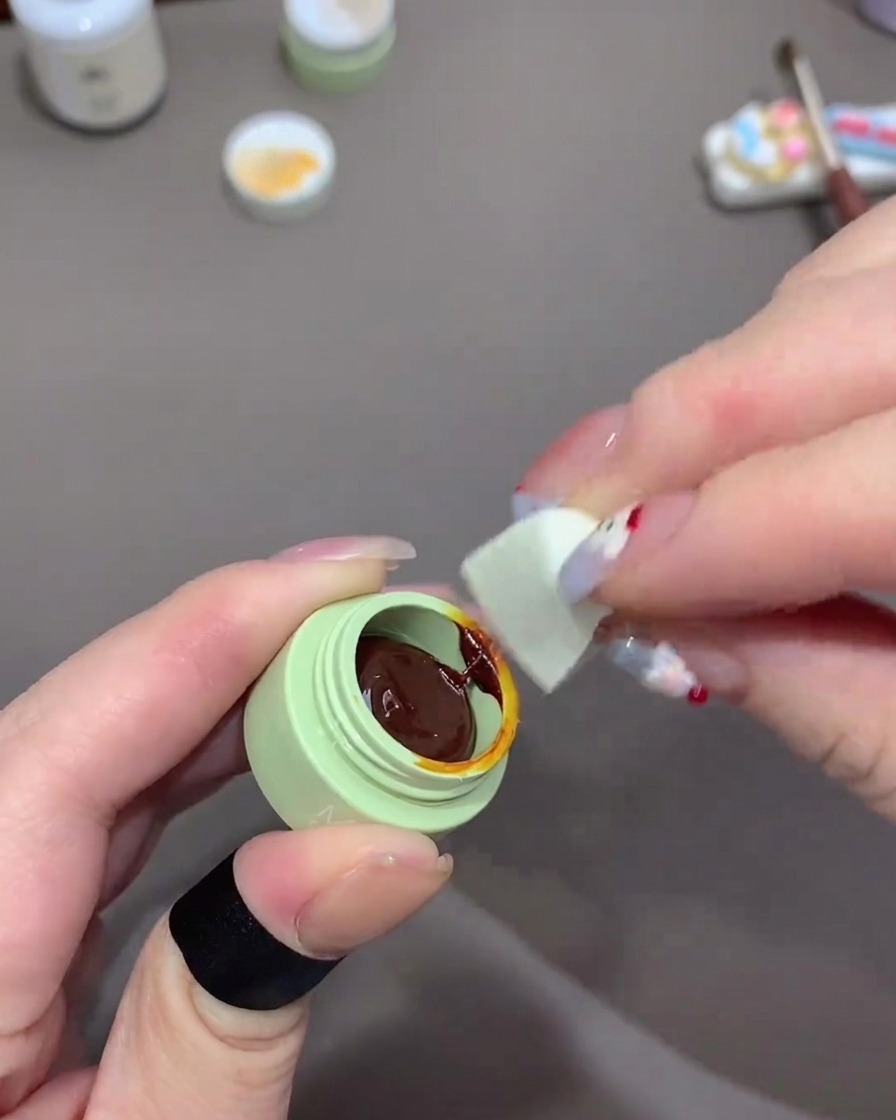 小さなグリーンのトレイから、メイク用スポンジを使ってクリアオレンジのジェルを少量含ませている様子。