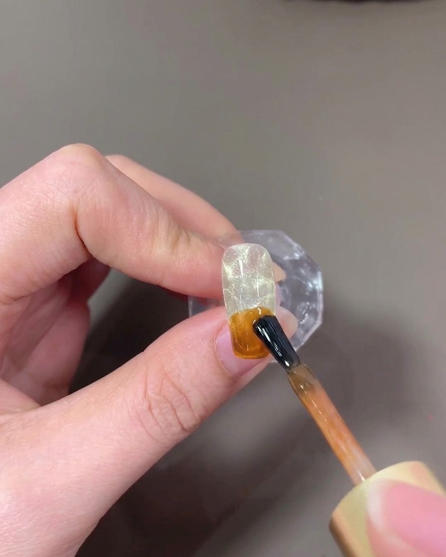 筆で爪の先に琥珀色の透け感ジェルを塗る様子。