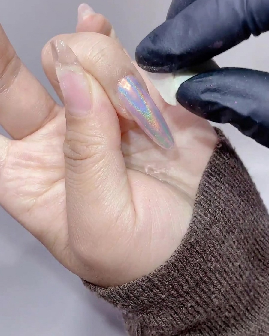 小さな白いメイク用スポンジを使って、長い爪の周りの皮膚についた余分なオーロラパウダーをきれいに拭き取っている手元のクローズアップ。