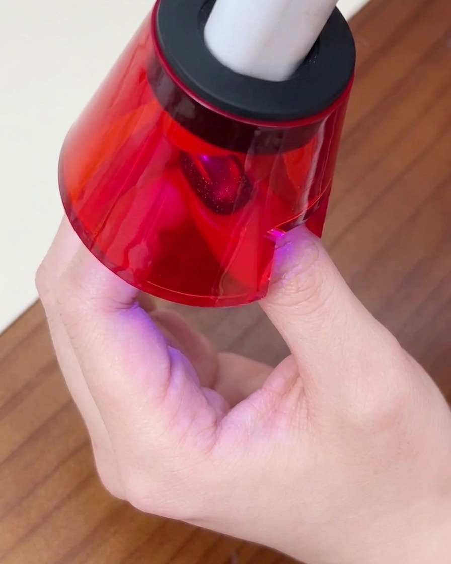 小型の赤いUV/LEDネイルライトの下に指を置き、最後のジェル層を硬化している様子。