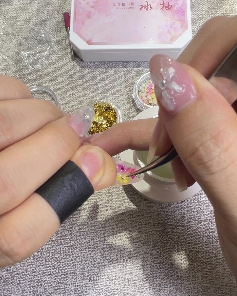 ピンセットを使って、爪の上の押し花の形や位置を整えている様子。