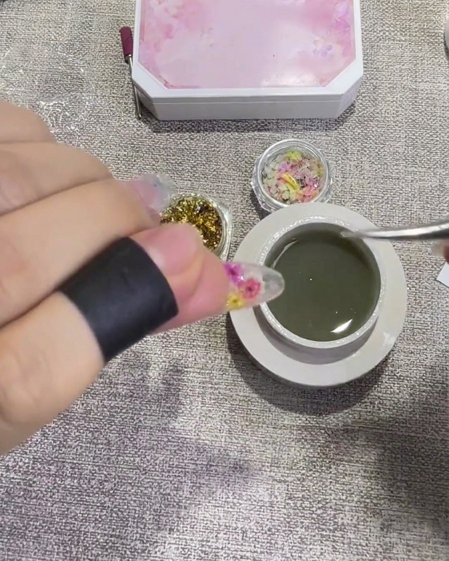 ピンセットで金箔をジェルに馴染ませるように押さえ、爪の表面に密着させている様子。