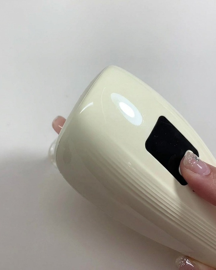 ヌードカラーを塗った爪の上に小型のポータブルUV/LEDライトをかざしてジェルを硬化させている様子。