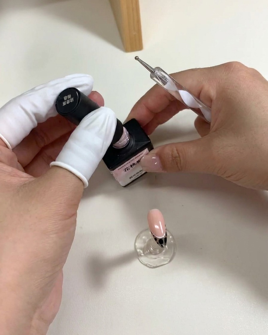ドットペンを使って、爪の表面にピンク色のジェルドットを5つ円状に配置し、花の形を作っている様子。