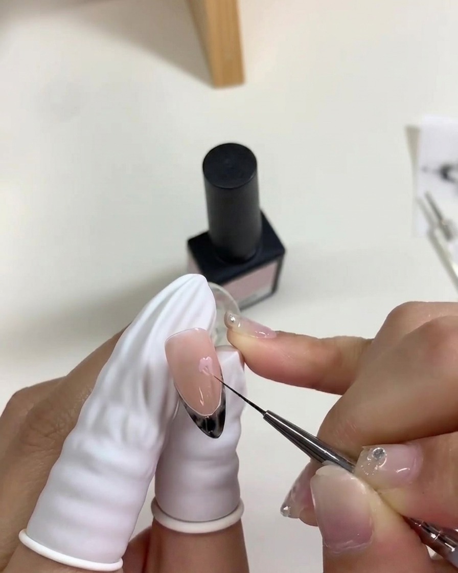 細いブラシを使って、濡れたピンクのドットの端を内側に引き寄せ、花びらの形を作っている様子。