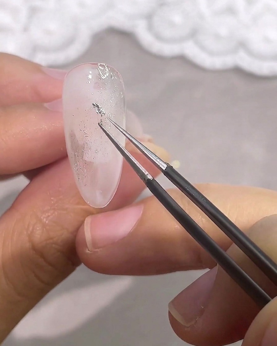 ピンセットを使って不規則な形の小さなシルバーホイルを爪に乗せる様子