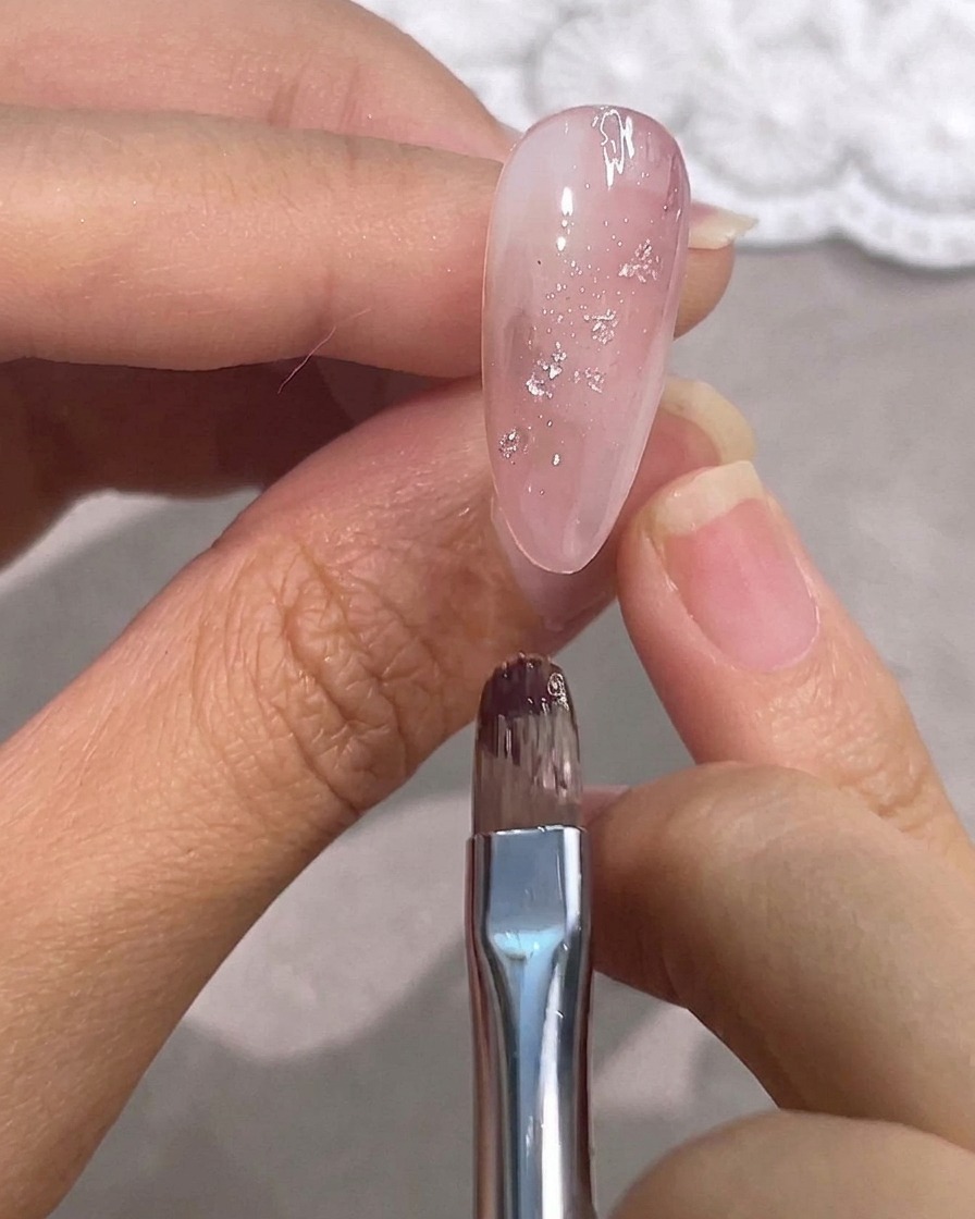 シルバーホイルが輝く艶やかなピンクのジェルネイルの上で作業する細筆