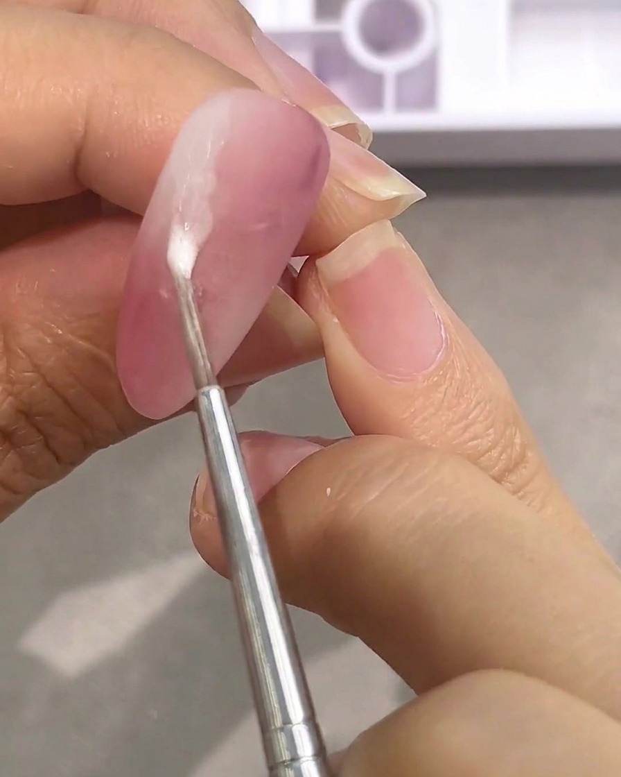 マットなピンクのネイルに、水分を多く含んだ白い絵の具をドロップする小さなツール