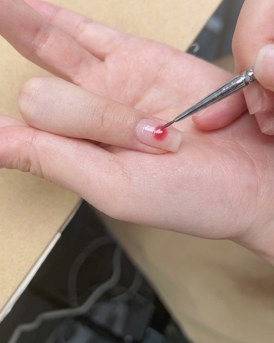 細筆でピンクドットの外側を優しくぼかし、チークのようなグラデーションを作っている様子。