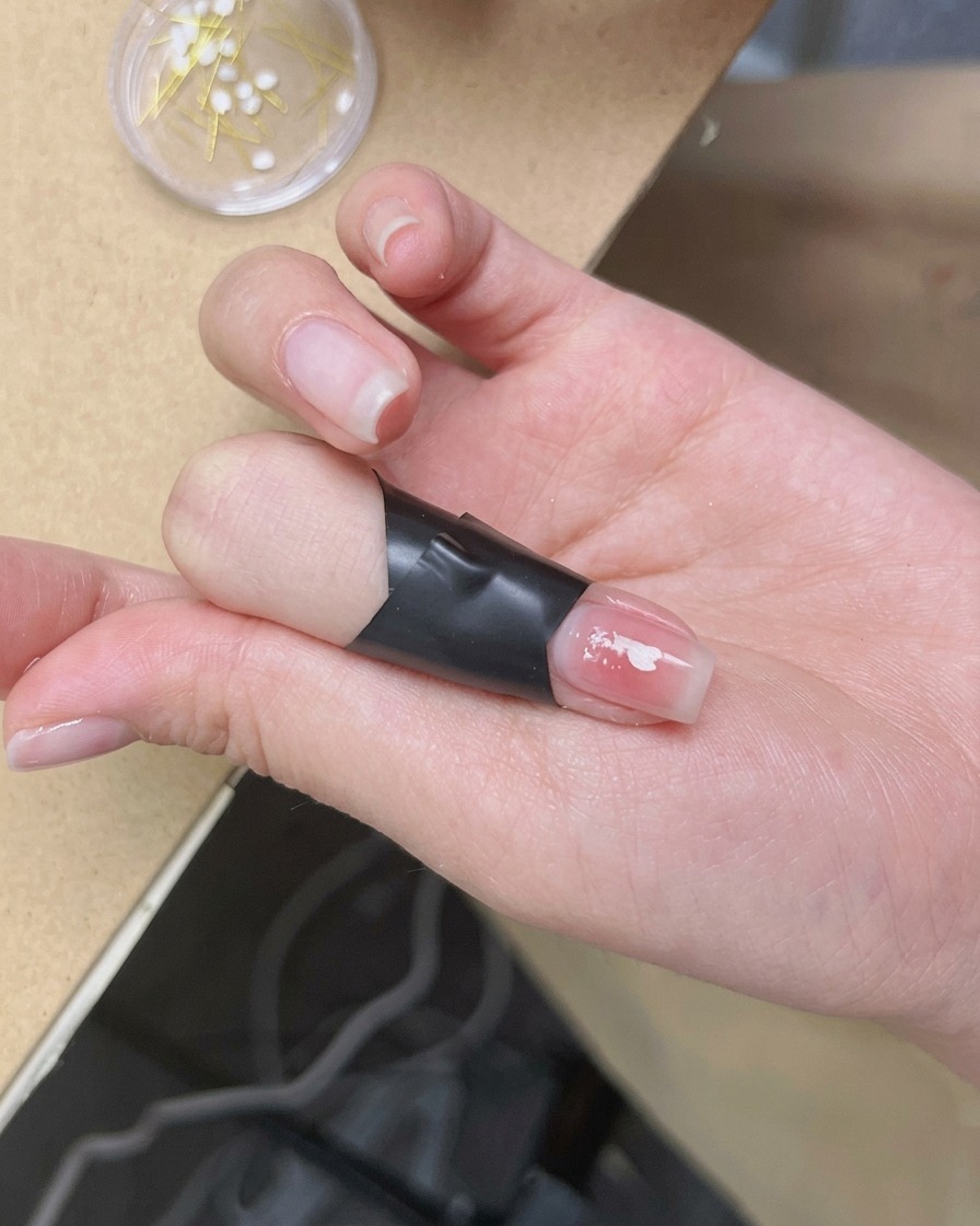 ピンセットで小さな白い桜のパーツを、爪の接着剤の上に丁寧に置いている様子。