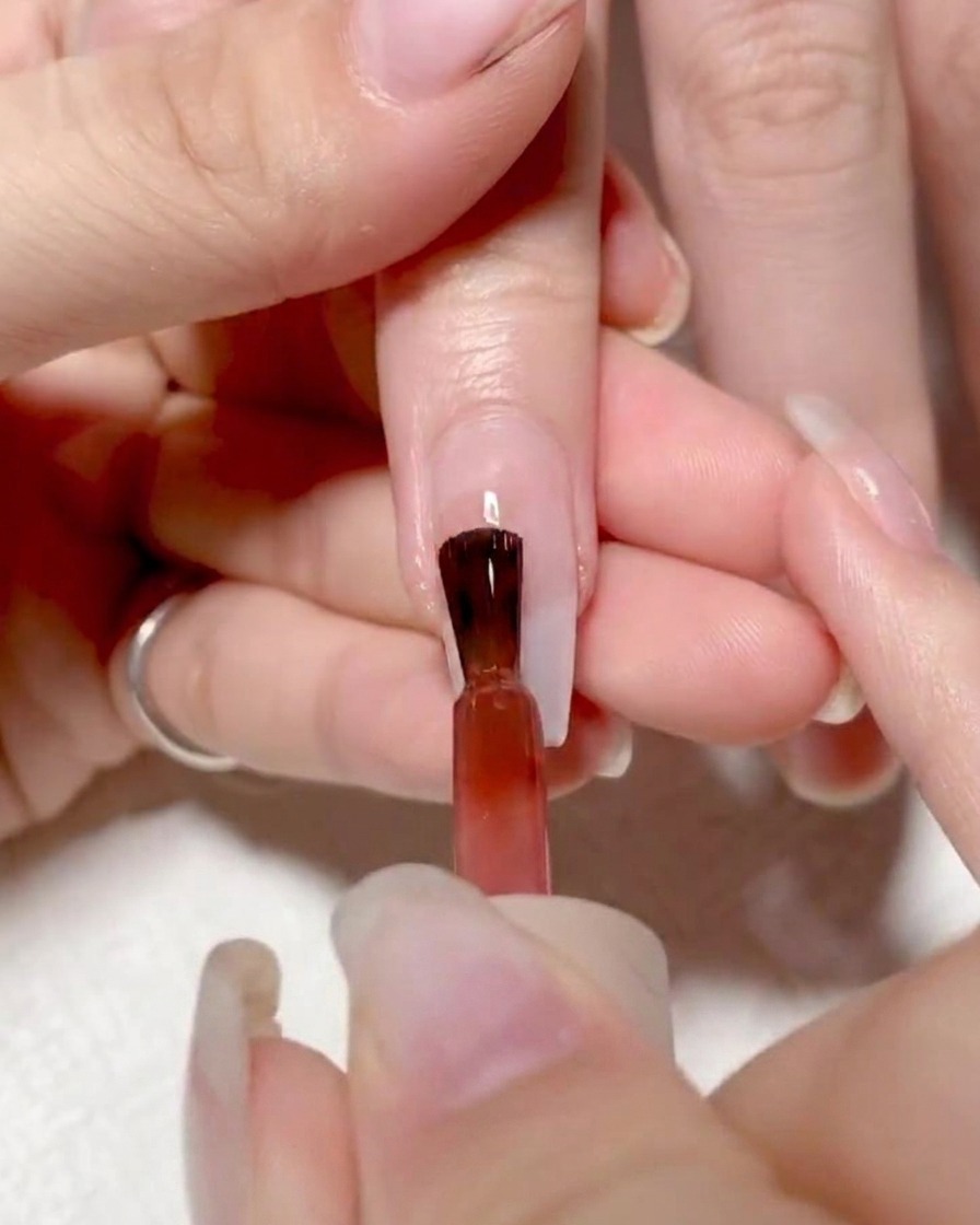 爪の左半分に鮮やかな赤のジェルを塗布している様子。