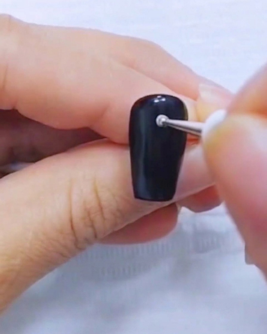 黒いネイルにドットペンで小さな白いドットを置いているアップ画像。