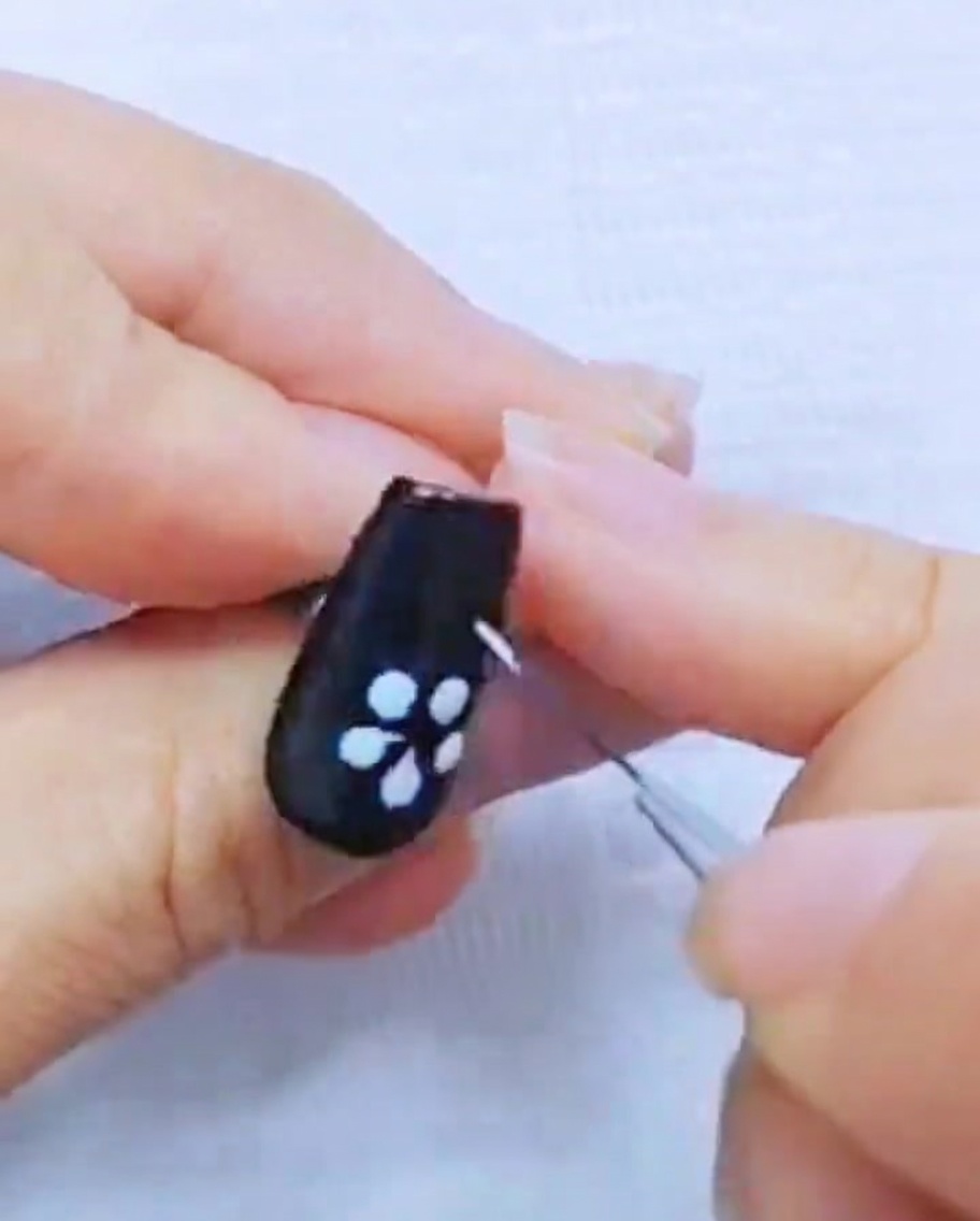 黒いネイル上の白いジェルの花びらをライナーブラシで整えているアップ画像。