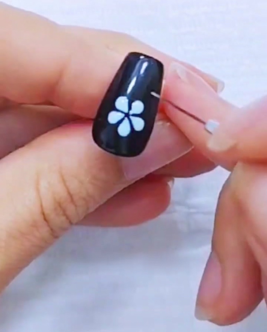 黒いネイルに描かれた白い5枚花びらのフラワーデザインの縁をライナーブラシで整えているアップ画像。
