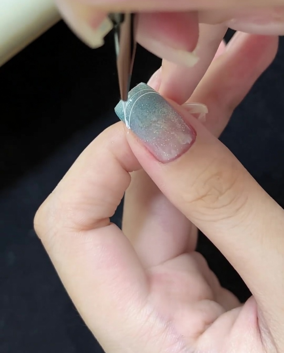 ブルーのキャッツアイネイルの先端の右角に、細い白い曲線を描く様子。