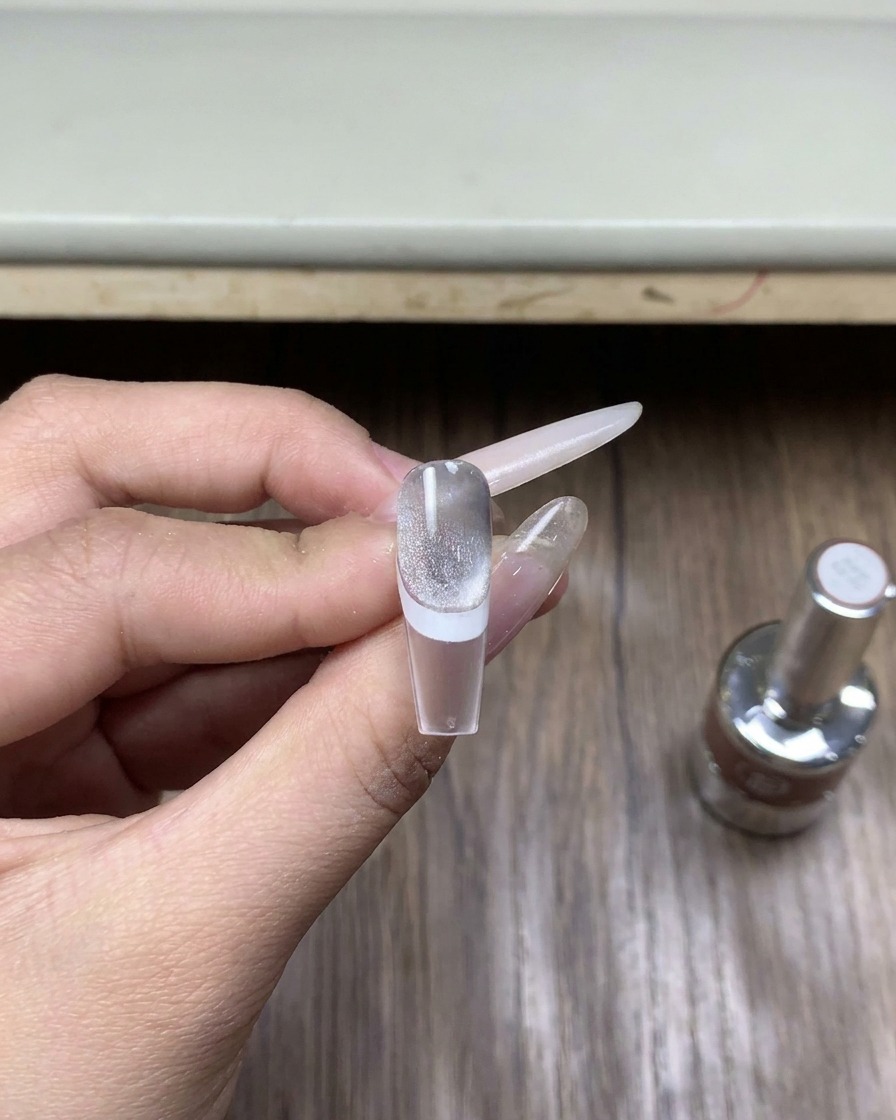 木の机の上に置かれた、クロムパウダー専用トップコートジェルの小さなガラスボトルのクローズアップ。