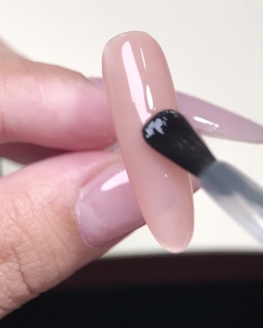 ピンセットを使って、ヌードカラーのネイルの上にフレンチ用シールを配置している様子。