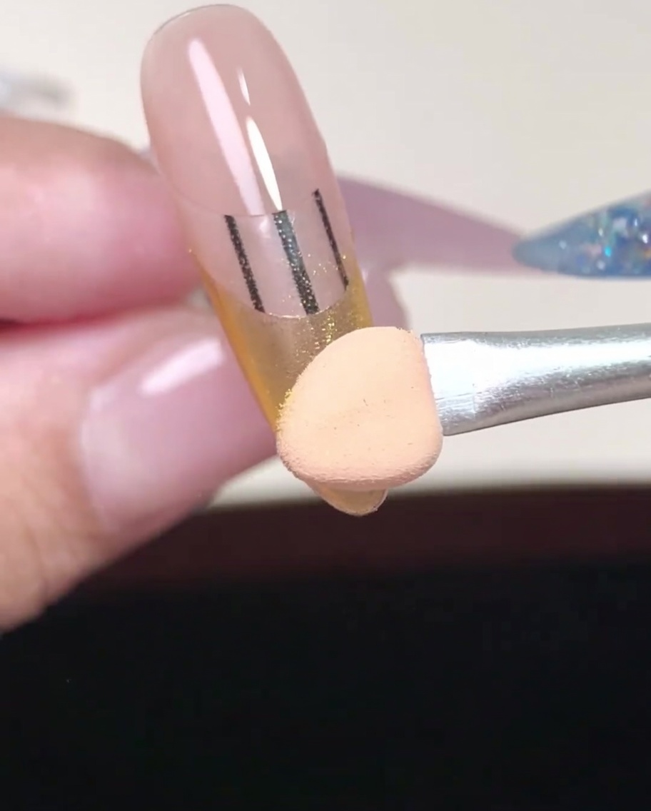 チップの先を使って、フレンチラインの角部分にゴールドパウダーを念入りに塗り込んでいる様子。