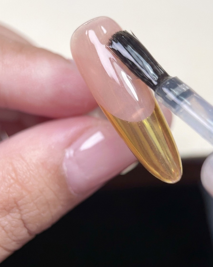 ゴールドのフレンチネイルを施した爪に、最後のトップコートを塗っている様子。