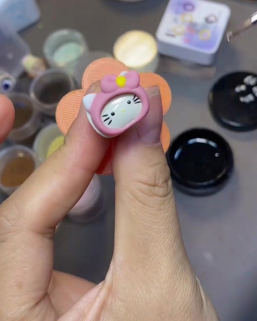 細いネイルアート用ブラシで、3Dハローキティのパーツにクリアトップコートを塗っている様子。
