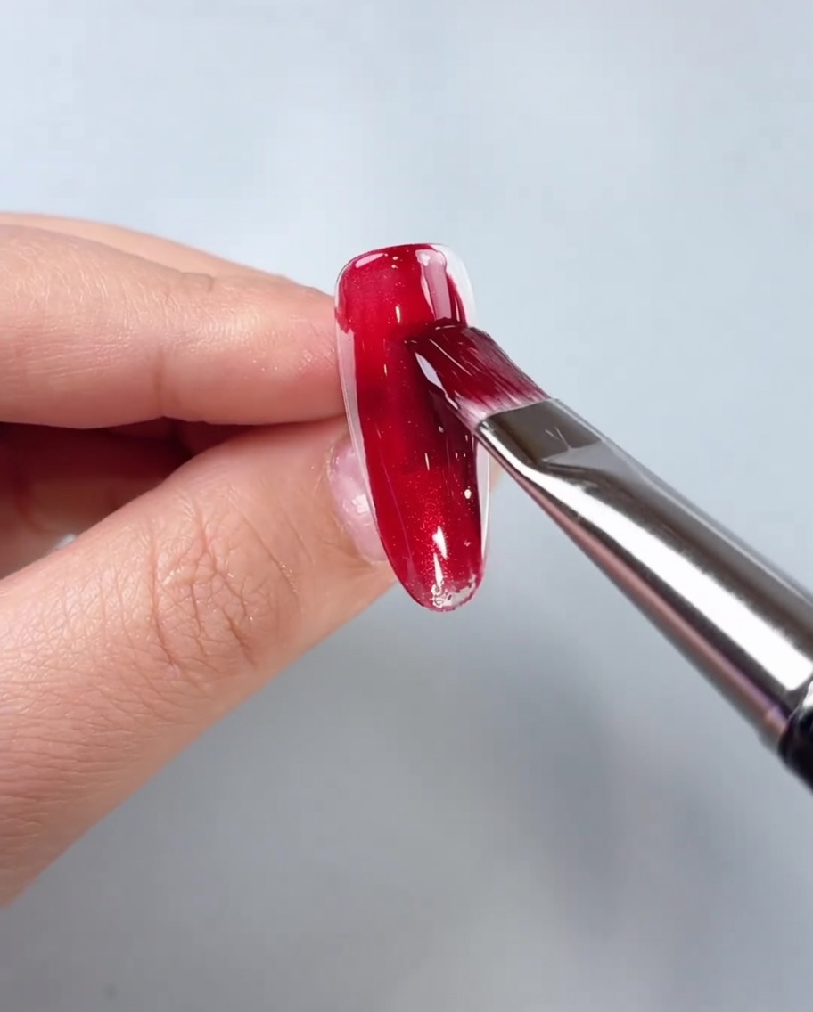 クリアのネイルチップの中央にレッドのマグネットジェルを筆で塗布している様子。
