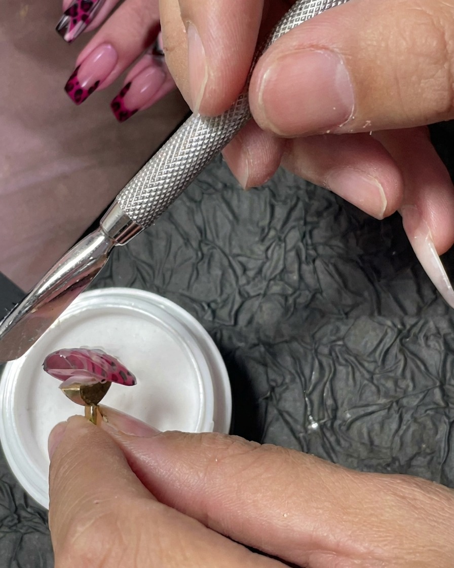 ピンクのネイルに乗せた濡れた赤のジェルに、白いアクリルパウダーを振りかけている様子。