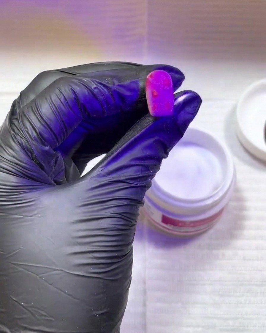 黒いグローブをはめた手が、紫色のUV/LEDライトの下でネイルを硬化させている様子
