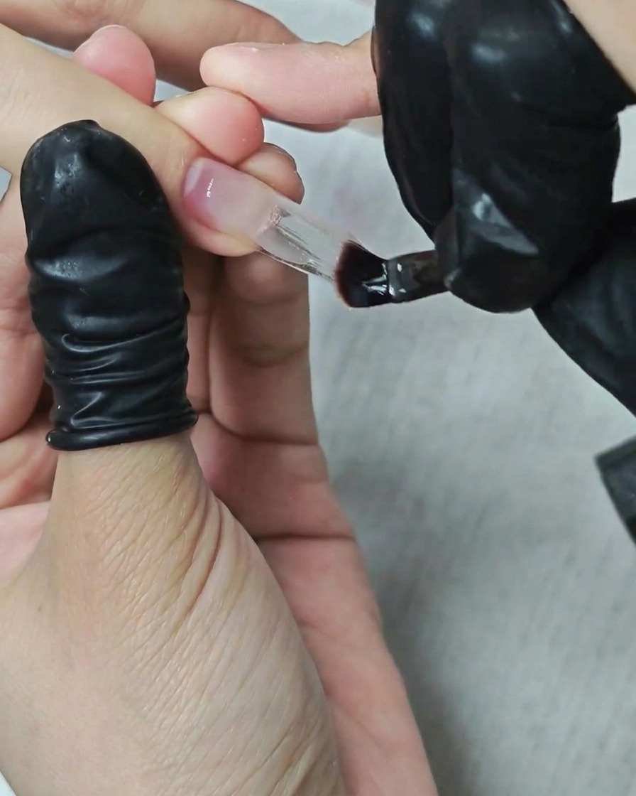 平筆を使用して、スクエア型の長さ出しネイルにクリアなビルダージェルをのせ、形を整えている様子。