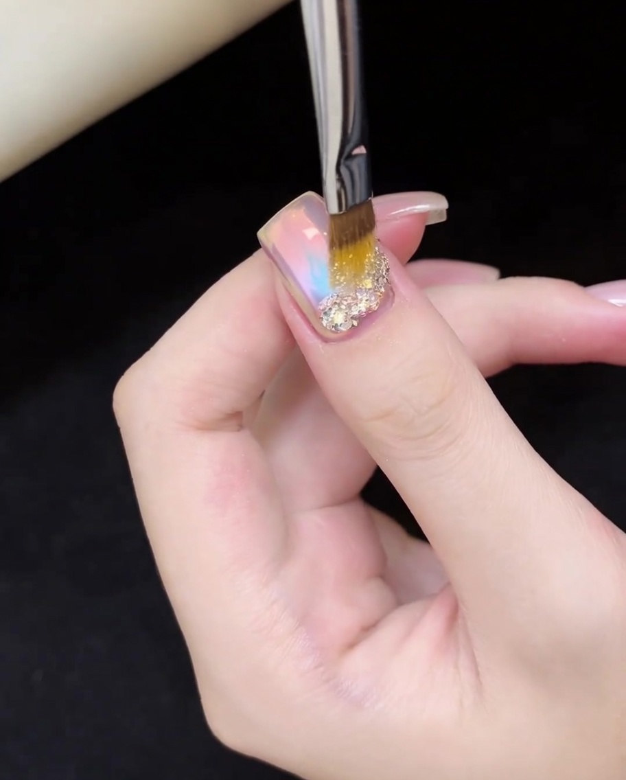 細い筆で虹色のグリッターを爪の根元に丁寧に配置している様子。