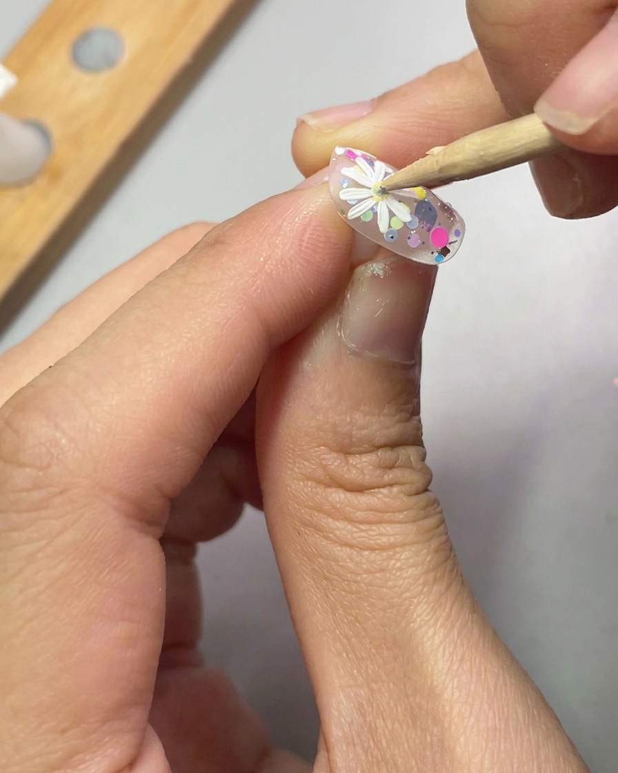 ドットペンを使い、白いデイジーの中心に黄色いジェルを乗せている様子。