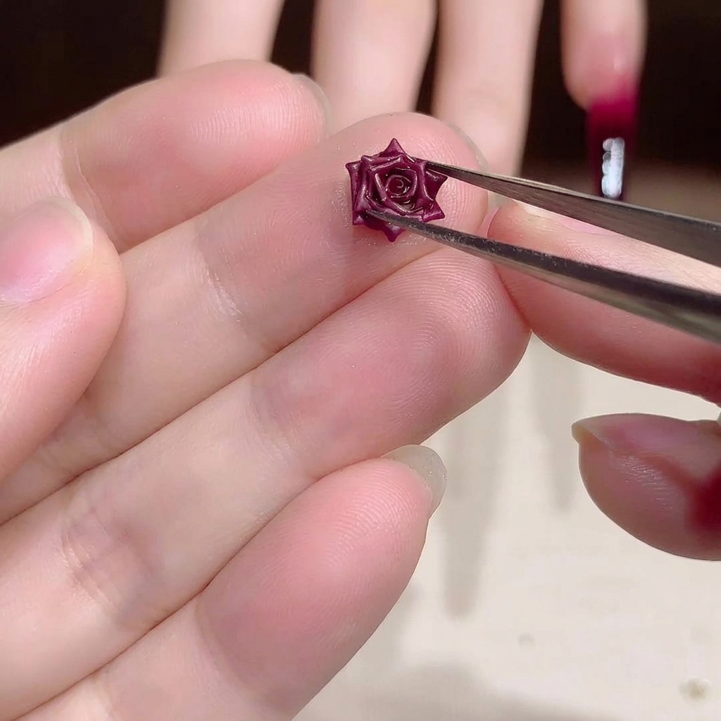金属ピンセットで、繊細なダークレッドの3Dドライフラワーチャームを慎重に持っているクローズアップ画像。