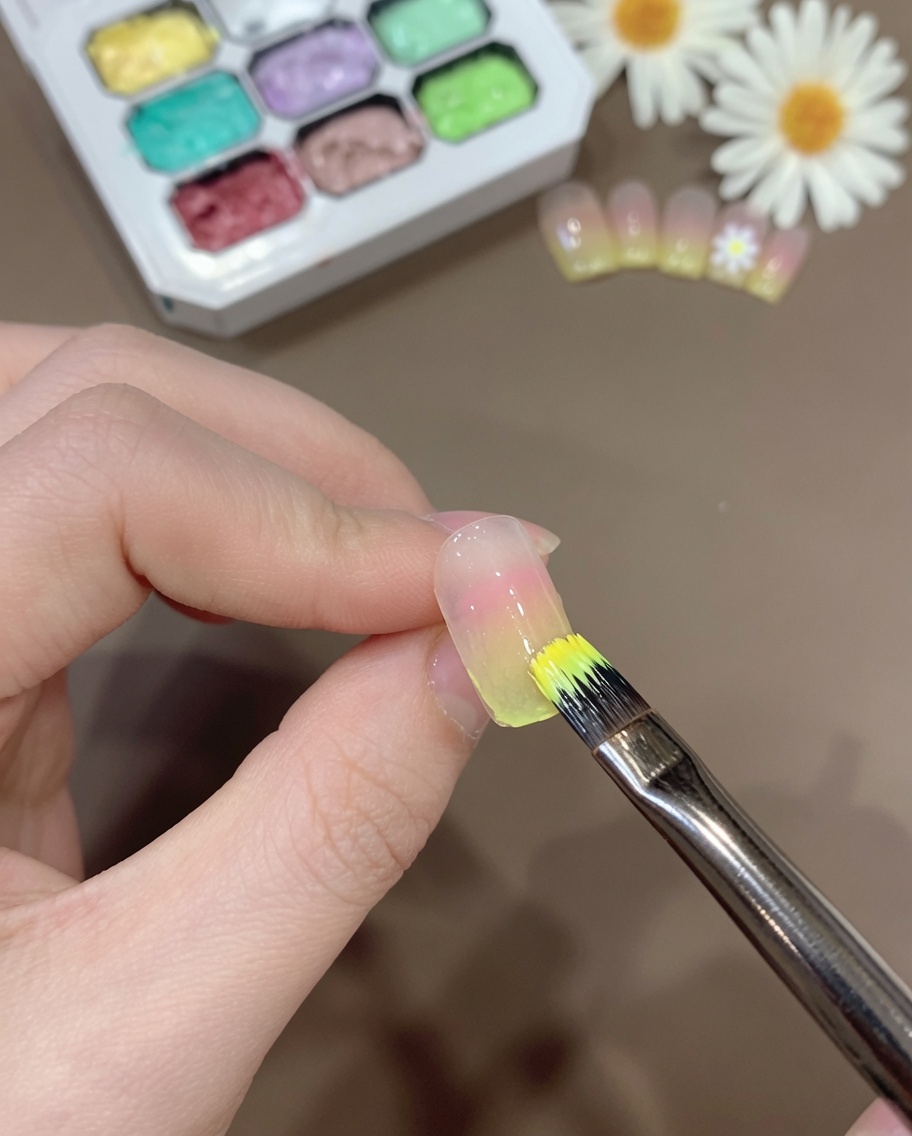 グラデーションの爪先に、混ぜ合わせた透け感のあるイエロージェルをブラシで薄く塗っている様子。