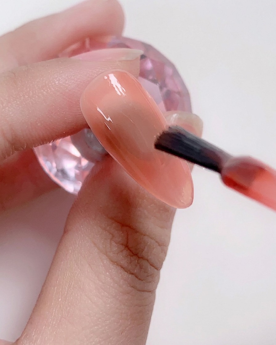 ライトピンクのジェルを爪全体に塗っている様子。