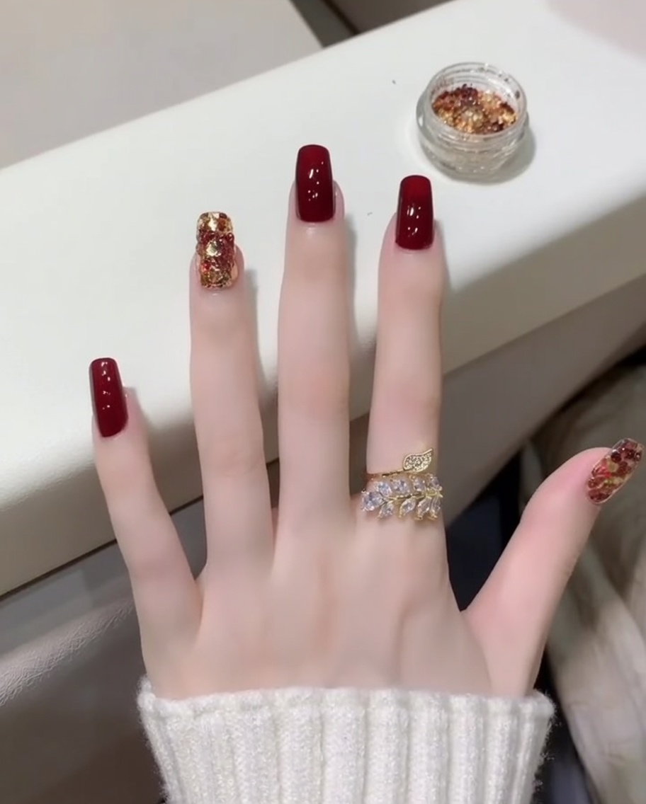 ダークレッドとグリッターのアクセントネイルの上から、クリアでツヤのあるトップコートをブラシで塗布しているクローズアップ。