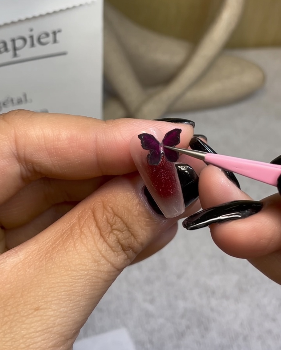 ピンセットでワインレッドの蝶のパーツをグラデーションネイルに乗せている様子