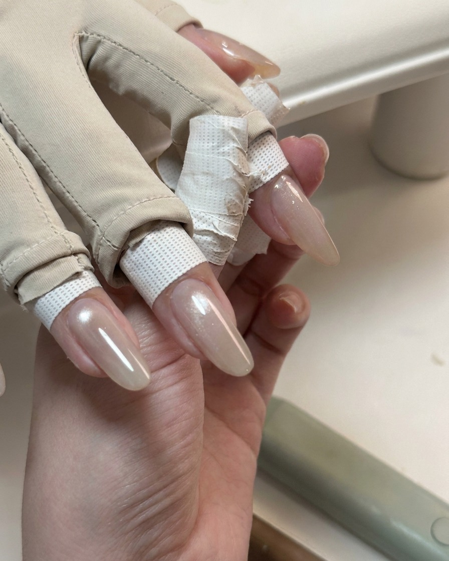 光沢のある半透明のキャッツアイジェル層で覆われたロングネイルの手元。