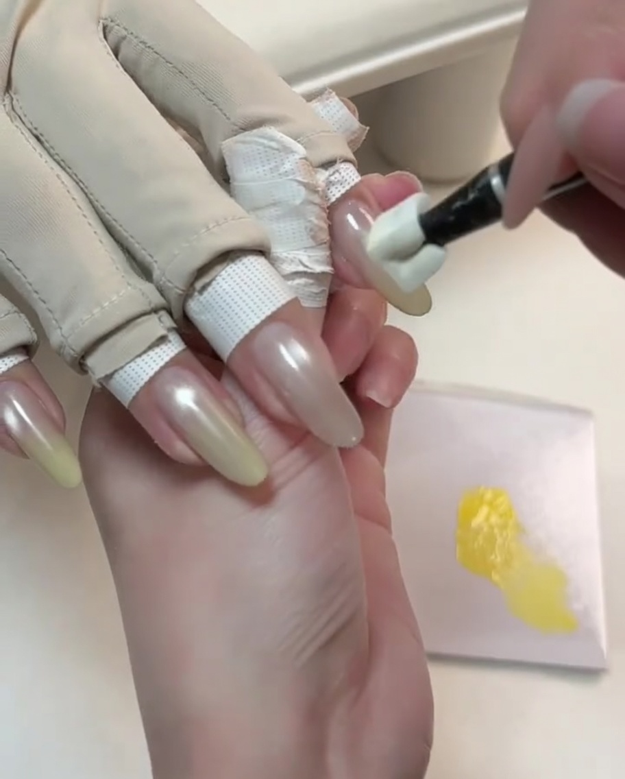 グラデーションを開始するため、ヌードキャッツアイネイルの先端に専用ツールでイエローのジェルをポンポンと乗せているところ。